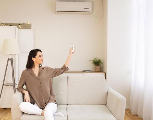 Young woman switching on air conditioning sitting on sofa
